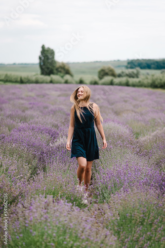Fototapeta Naklejka Na Ścianę i Meble -  Beautiful woman funny walk on the lavender field on sunset. Beautiful girl in dress stand and flying long hair on purple lavender field. Soft focus. Enjoy the floral glade, summer nature. Hairstyle.