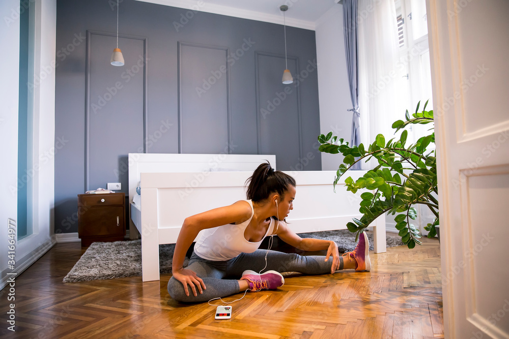 Slim sportswoman in sportswear doing stretching exercise before workout while sitting on floor at home Slim sportswoman in sportswear doing stretching exercise before workout while sitting on floor at home