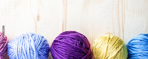 Multicolored woolen balls on wooden background. Banner with botten border. Knitting as hobby. Purple, yellow and blue woolen tubes.