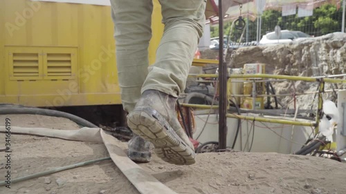 Man walking through working industrial site. Follow shot to a male worker feet in boots. engineering Legs of young man stepping on hose and cables Low angle view Close up Slow motion