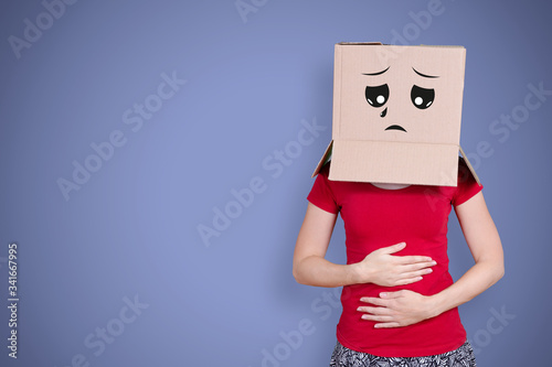 Person with cardboard box on its head and a sad face expression holding ist belly on purple background