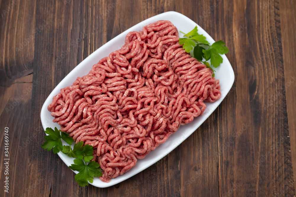 ground meat on white dish on brown wooden background ground meat on white dish on brown wooden background
