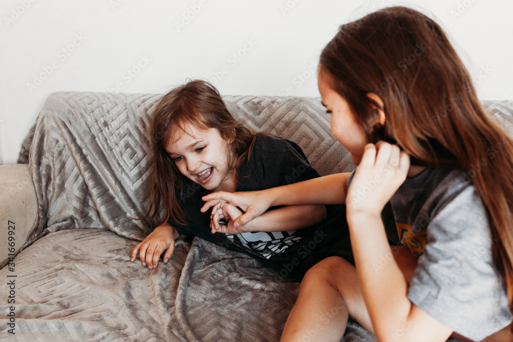 Two little girls, sisters playing at home, jumping on the couch, hugging, kissing each other, fighting, arguing, isolation, vacation, weekend at home, communication Two little girls, sisters playing at home, jumping on the couch, hugging, kissing each other, fighting, arguing, isolation, vacation, weekend at home, communication