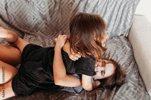 Two little girls, sisters playing at home, jumping on the couch, hugging, kissing each other, fighting, arguing, isolation, vacation, weekend at home, communication