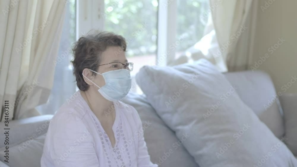 Happy beautiful older middle aged woman wearing protective mask relaxing sitting on sofa at home, stay at home health care COVID-19 pandemic situation. Happy beautiful older middle aged woman wearing protective mask relaxing sitting on sofa at home, stay at home health care COVID-19 pandemic situation.