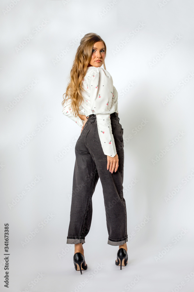 Beautiful blonde model posing in white shirt with floral design and jeans in studio Beautiful blonde model posing in white shirt with floral design and jeans in studio