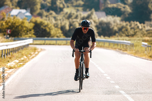 Front view of active man in sport clothing, black helmet and mirrored glasses riding professional bike on nature during summer time. Concept of active lifestyle