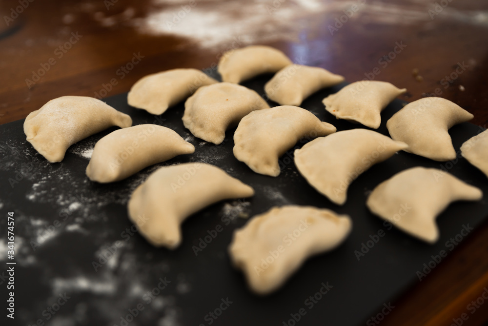 Uncooked russian vareniki on cutting wooden board with flour on baking paper. Process of making vareniki. top view.Typical Eastern European food, called dumplings, dumplings, dumplings, pies or pies Uncooked russian vareniki on cutting wooden board with flour on baking paper. Process of making vareniki. top view.Typical Eastern European food, called dumplings, dumplings, dumplings, pies or pies