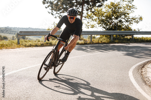 Bearded cyclist in sport clothing, protective helmet and mirrored glasses riding black bike among countryside nature during summer time. Mature man preparing for competitions and races. photo