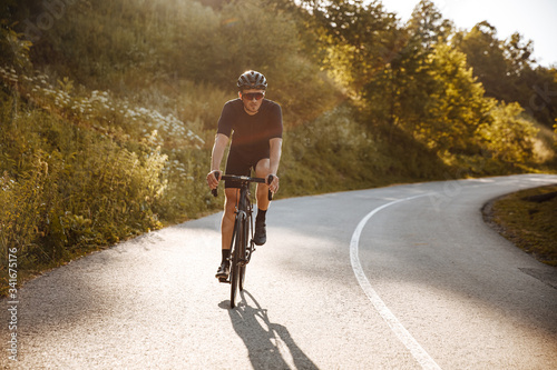 Professional cyclist wearing sport clothing, black helmet and mirrored glasses riding bicycle and workout on fresh air. Mature man doing sport activity on nature.