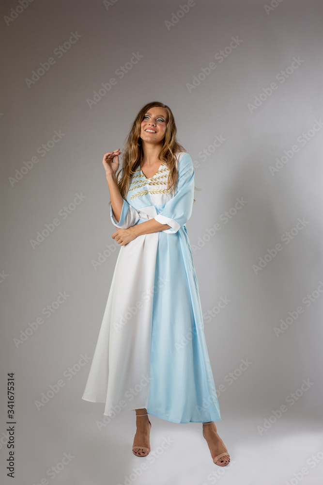 Beautiful blonde woman posing white and blue dress with golden details