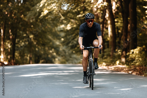 Mature bearded man in active wear and protective helmet dynamically riding bike on paved road. Bicyclist in mirrored eyeglasses enjoying favore hobby on fresh air. © Tymoshchuk
