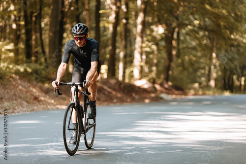 Mature bearded cyclist in activewear, black helmet and mirrored glasses riding bicycle with beautiful nature around. Concept of summer activity and healthy lifestyle