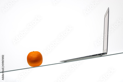 laptop in a white office on a glass table with an orange on a white background