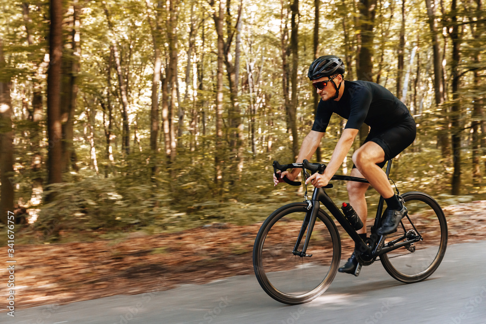 Side view of mature man with sporty body in protective helmet practising in cycling outdoors. Bearded athlete wearing mirrored glasses biking on asphalt road Side view of mature man with sporty body in protective helmet practising in cycling outdoors. Bearded athlete wearing mirrored glasses biking on asphalt road