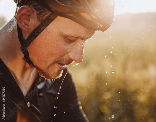 Canvas Print Close up portrait of tired bearded athlete in protective helmet with water drops on his face