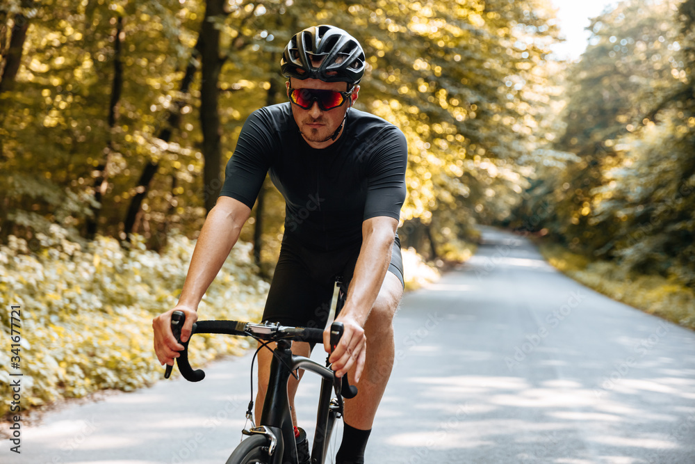 Obraz premium Bearded man with athletic body shape wearing sport clothing and mirrored glasses, riding bicycle among green forest. Concept of active and healthy lifestyle