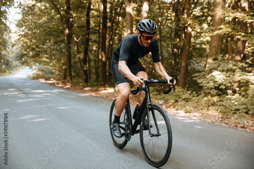 Active bearded man in sport clothing and black helmet riding bicycle with beautiful nature around. Mature cyclist in mirrored glasses doing favorite hobby outdoors.