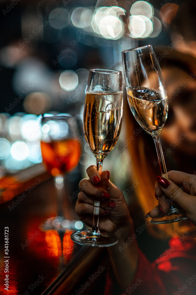 The girls at the bar clink glasses with sparkling wine. Clinking champagne glasses with friends. The atmosphere of a night club. Close-up of hands