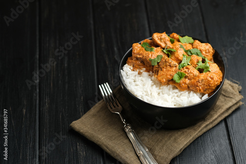 Chicken tikka masala traditional Asian spicy meat food with rice tomatoes and cilantro in a black bowl on dark background.