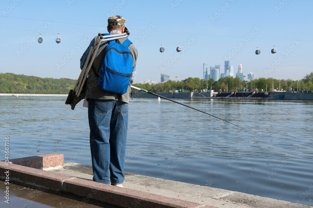 Fisherman on the bank of Moscow river on the background of Moscow city and cable car at Vorobyovy Gory.