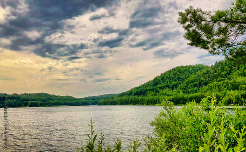 A forest lake under a colorful and dramatic sunset or sunrise sky seen from between the trees and foliage of the forest