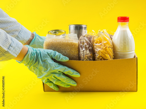 Wallpaper Mural Food staples delivery or donation box concept on yellow background. Safe alimentary delivery during coronavirus pandemic. Hands in blue medical gloves holding the box. Torontodigital.ca