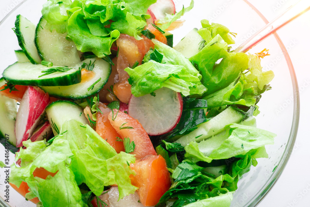 fresh salad in a bowl with tomatoes, cucumbers, lettuce radish, olive oil and sesame seeds close-up selective focus