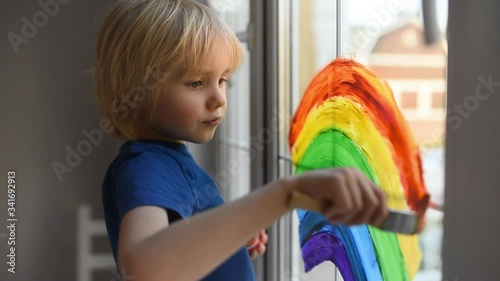 Little boy drawing rainbow on  window while coronavirus quarantine. Rainbow sign is symbol of hope, means that everything will be OK. Stay at home for lockdown coronavirus. photo