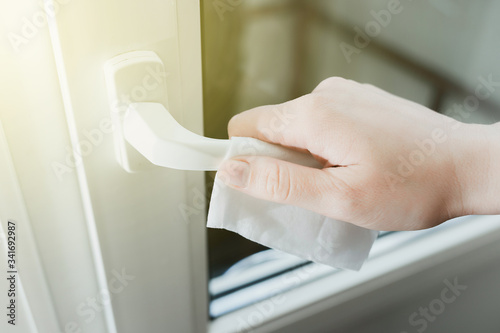 closeup female hands with a wet towel wipe the handle of a white door from viruses