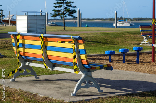 Lonely colourful park bench taped up for public safety looking out to a boat in the sea during Covid-19 crisis on the Gold Coast, Australia.