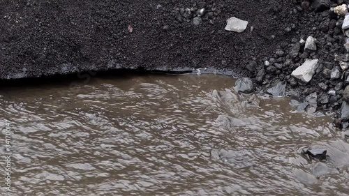 Glacier with ash in the ice with melted water and Icelandic landscape. Little trickle because of melting ice of a glacier in Iceland