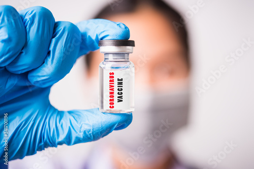 woman doctor or scientist wearing face mask protective in lab use hand finger hold vial vaccine bottle