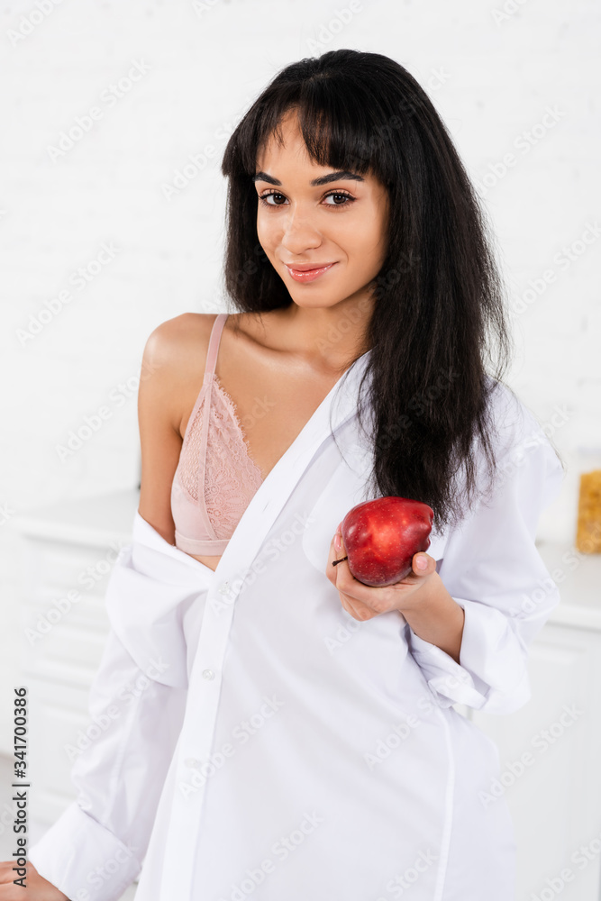 African american girl with apple smiling and looking at camera in kitchen African american girl with apple smiling and looking at camera in kitchen
