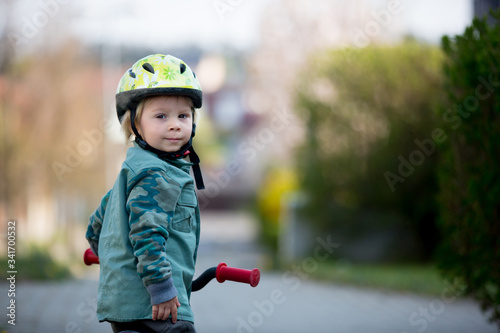 Blonde little toddler child in riding bike, wearing helmet and playing on the playground
