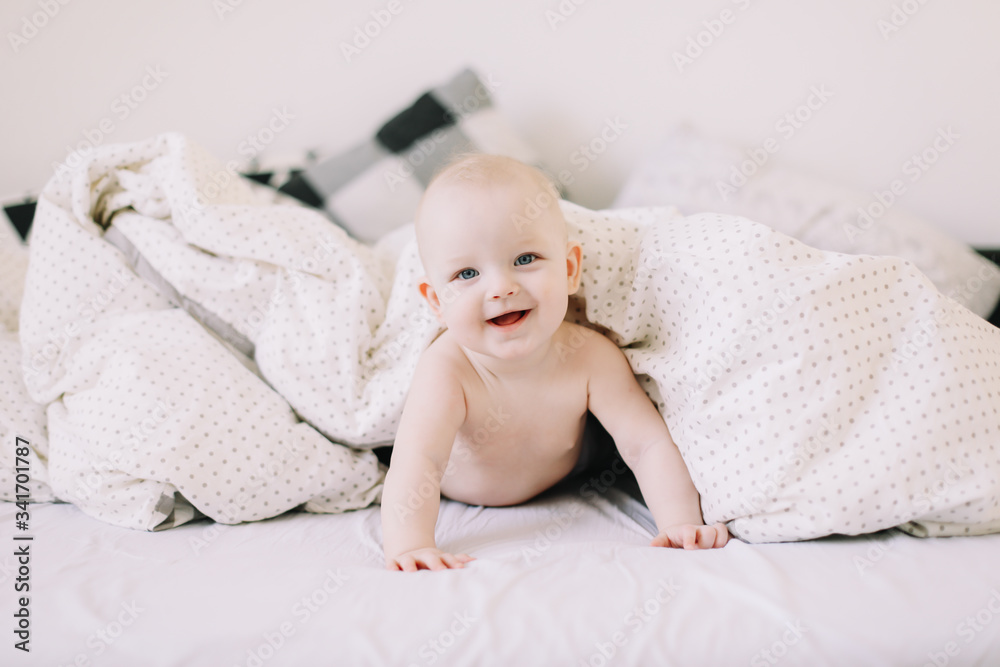 Portrait of a crawling happy baby on the bed under the blanket. Textile and bedding for kids. Childhood and baby care concept Portrait of a crawling happy baby on the bed under the blanket. Textile and bedding for kids. Childhood and baby care concept