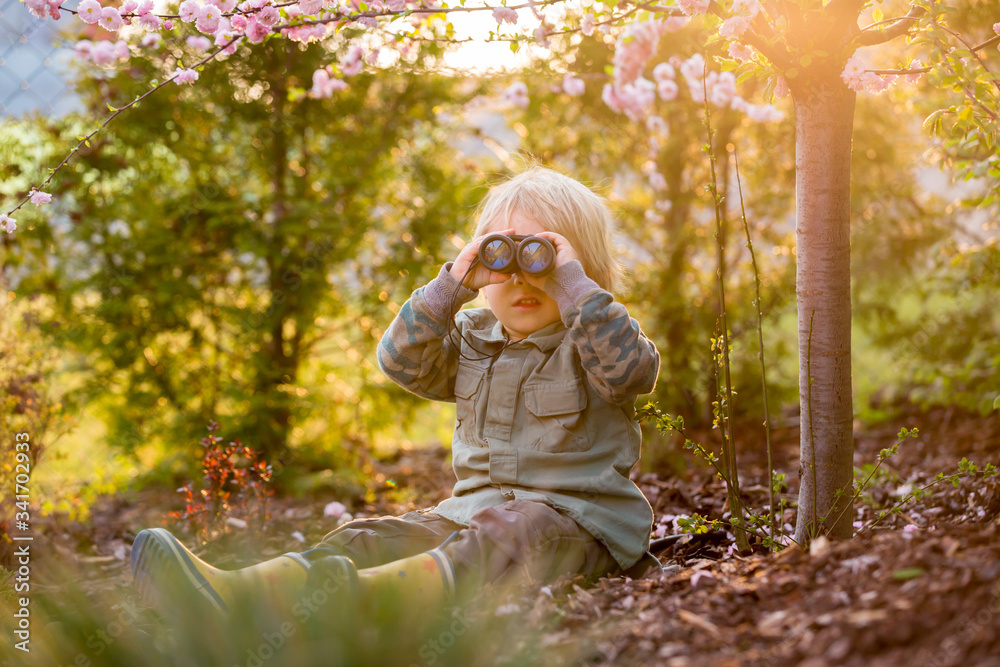 Blonde little toddler child with binoculars, sitting in garden on sunset