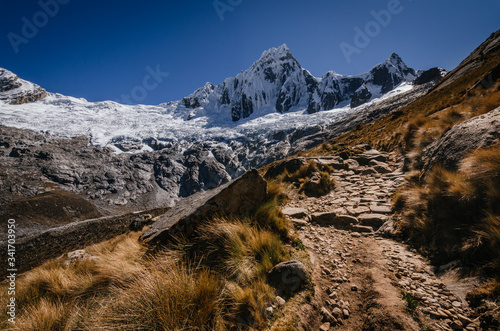 .High snowy mountain of Taulliraju and path surrounded by grass in the foreground, in the quebrada santa cruz in peru photo