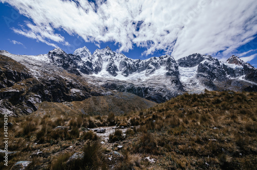 high snowy Taulliraju mountain surrounded by clouds and bushes in the foreground, in the Andes trekking of the quebrada santa cruz © Gorka Vega Barbero