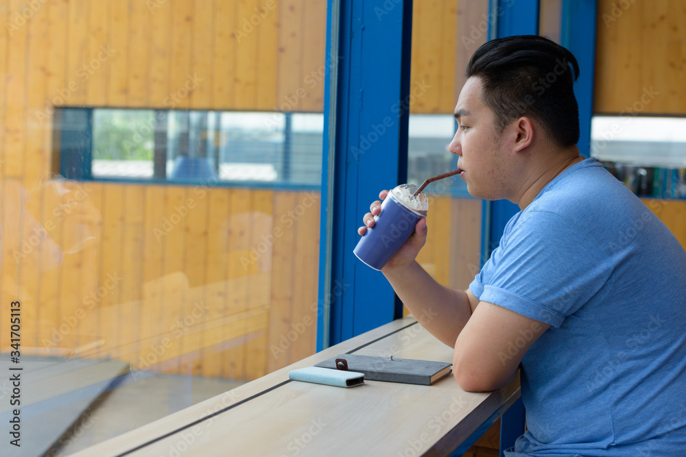 Young overweight Asian man drinking coffee at the coffee shop