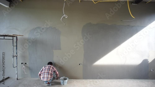 Back portrait workers plastering the cement on the concrete wall by trowel in the house under construction.