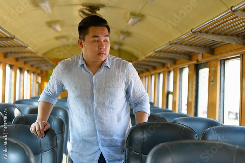 Young overweight Asian tourist man looking through window inside the train