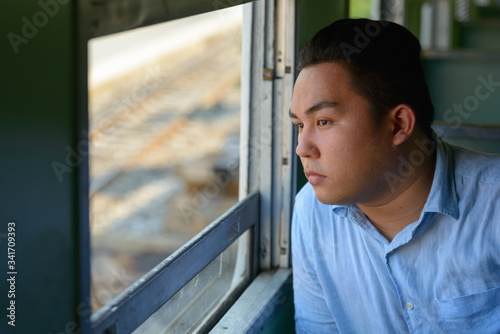 Young overweight Asian tourist man looking through window inside the train
