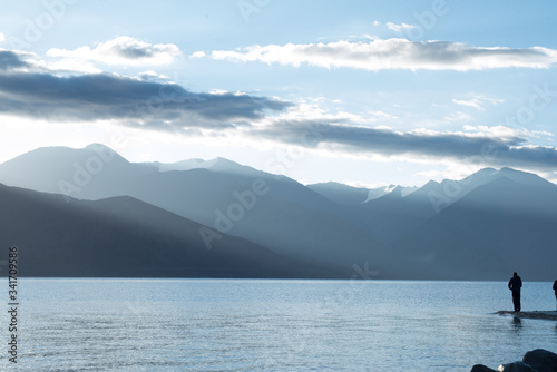 Mountains surrounding the lake. This is an early morning landscape of the scene. Sun rays are trying to enter casting long shadows or clouds and mountains on to the lake.