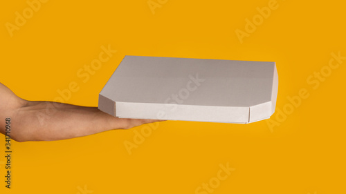 Unrecognizable delivery man holding box with takeaway pizza on orange background, mockup for design. Panorama