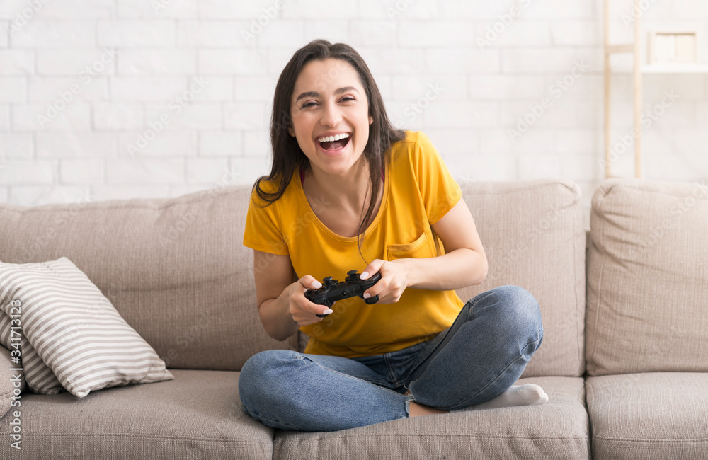 Fun stay home pastimes. Excited Hispanic girl with controller playing video games on sofa indoors Fun stay home pastimes. Excited Hispanic girl with controller playing video games on sofa indoors