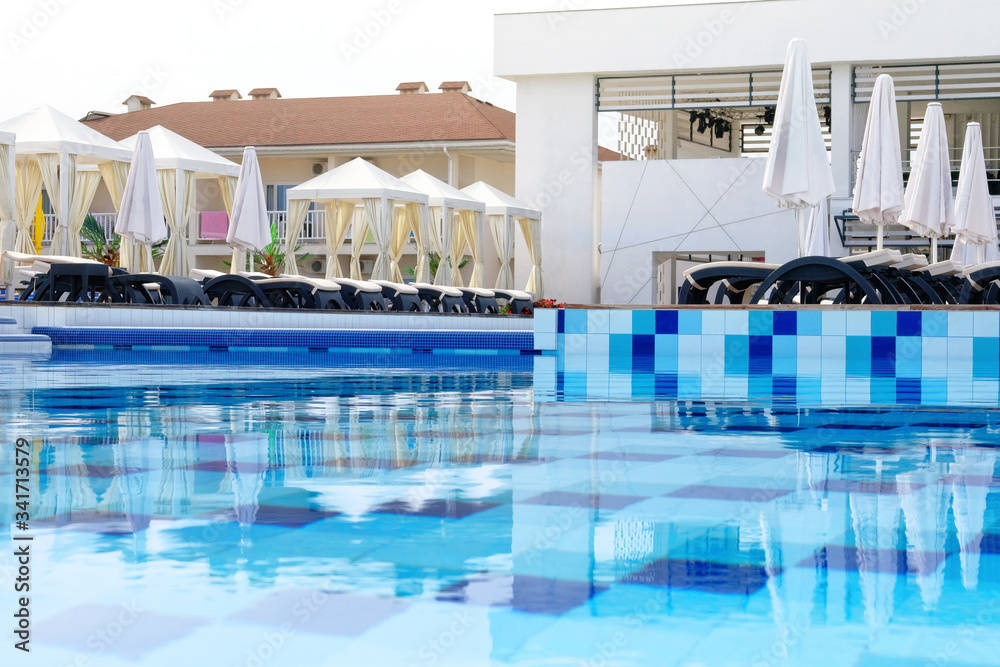 Aquatic swimming pool with sun loungers and beach umbrellas in luxury resort. Spa and relax in vacations and holiday.