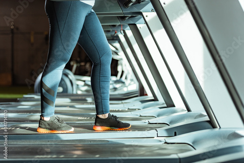 cropped view of overweight girl in leggings running on treadmill in gym