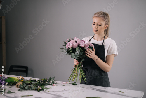 Professional young woman florist wearing apron making floral composition from fresh roses at the table on white background. Concept of working with flowers, floral business. photo