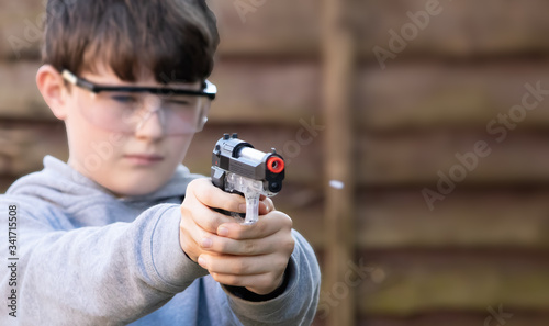 boy shoots white plastic bb pellet at target in garden with electric airsoft pistol